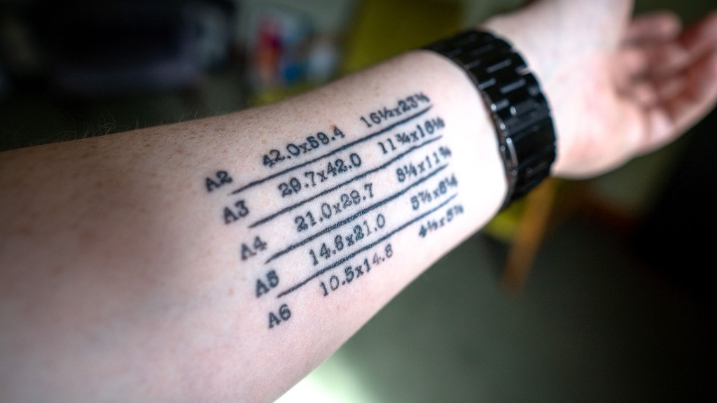 An arm tattooed with paper sizes